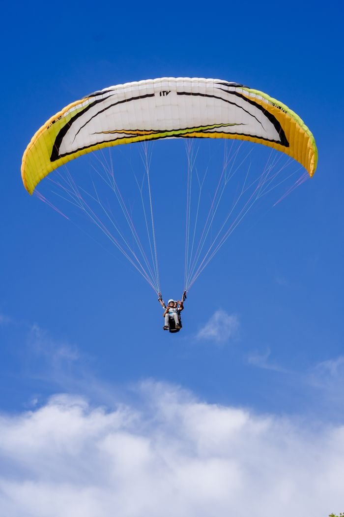 A paraglider enjoying the thrill of flight against a clear blue sky, evoking freedom and adventure.