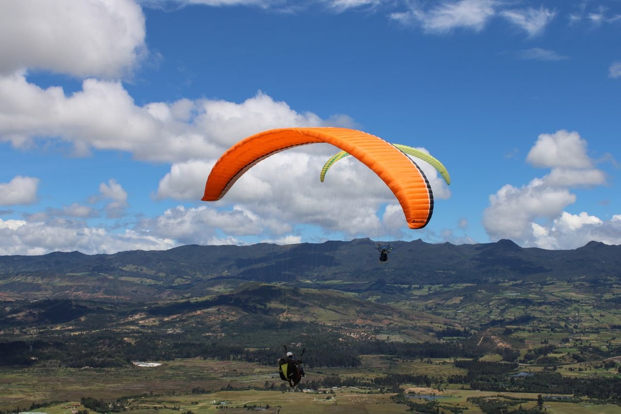 Experience the thrill of paragliding over a breathtaking mountain vista under a clear blue sky.