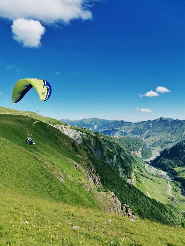 Experience thrilling paragliding over the stunning mountains of Gudauri, Georgia, with clear blue skies.